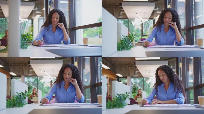摄像机跟踪显示女商人坐在办公室的办公桌上批准布局或样张-慢动作拍摄