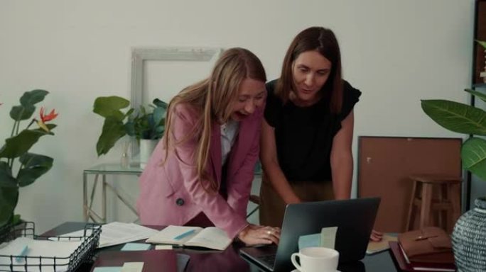 工作场所的女性领导力。两个漂亮的年轻高加索商人交谈，一起在办公室桌子上使用笔记本电脑。