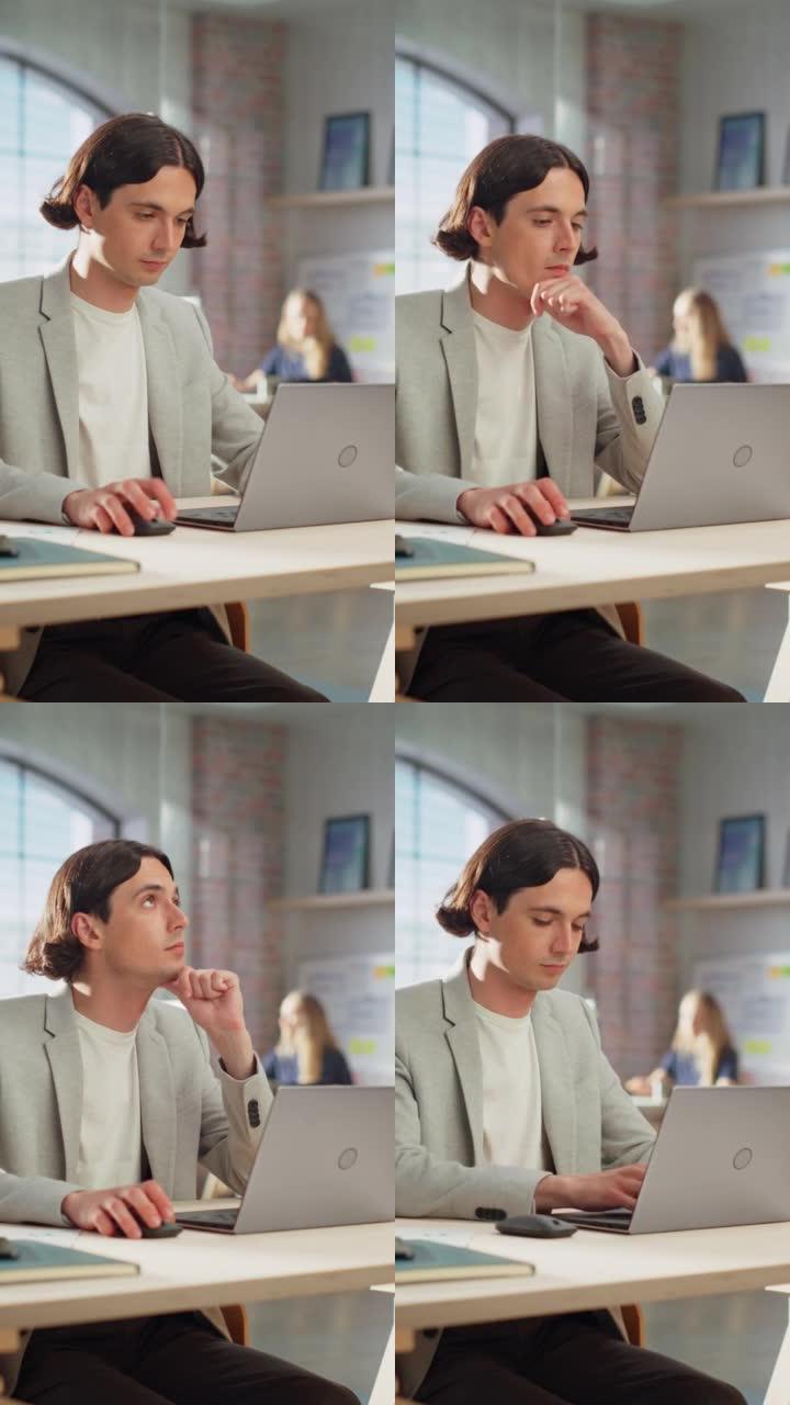 垂直屏幕: 英俊的经理坐在创意办公室的办公桌前。穿着夹克的年轻时尚男人在营销机构使用笔记本电脑。在后