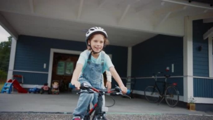 年轻的父亲教他的女儿在他们大房子的草坪上骑自行车。成功的女孩戴着头盔，在自行车上保持平衡和踩踏板。手