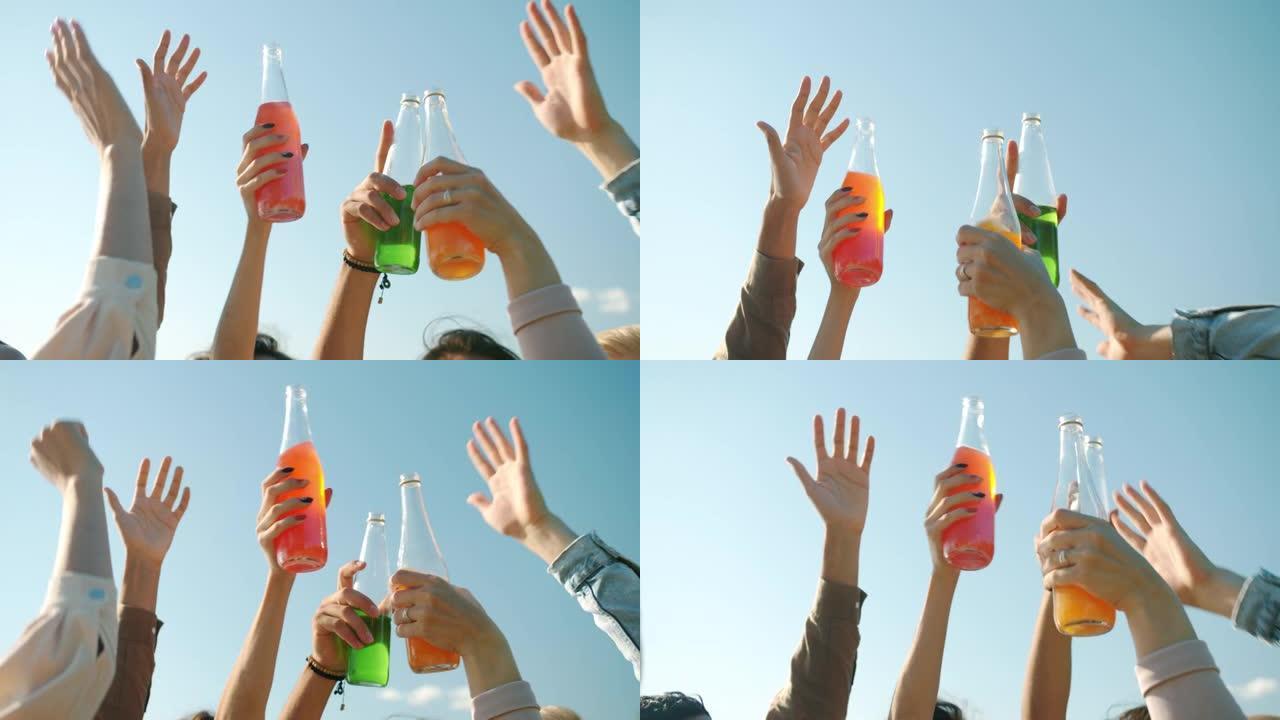 举起的男性和女性双手拿着酒瓶在户外跳舞的特写镜头
