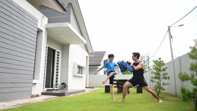 一名亚洲华裔父亲运动员在晚上的跆拳道比赛中训练他12岁的儿子在房子的前院
