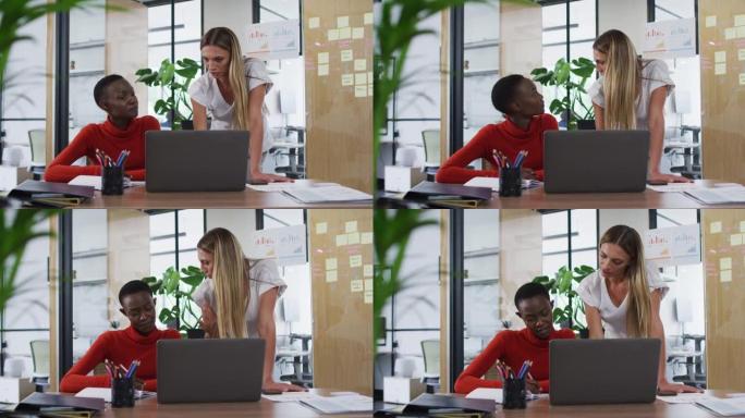 两位不同的女性办公室同事用笔记本电脑在办公室一起讨论