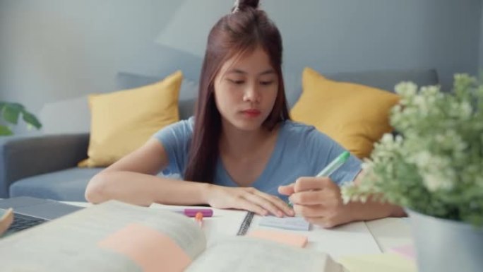 年轻的亚洲女孩十几岁的时候用笔记本电脑在家里的客厅里上网学习，为期末考试写讲稿。隔离教育在线电子学习