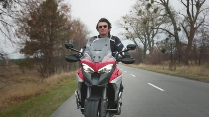 骑自行车的人骑着旅游摩托车在路上。英俊的男人驾驶时尚的红色摩托车。两轮旅行概念。慢动作镜头