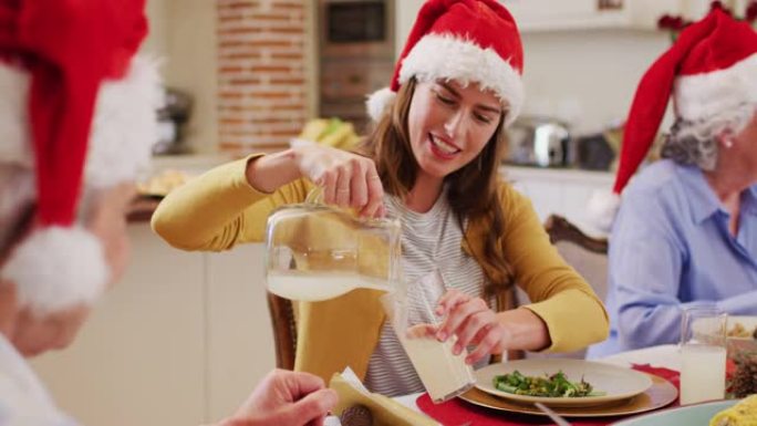 戴着圣诞老人帽子的白人妇女坐在餐桌上，在高级男子的杯子里倒着饮料