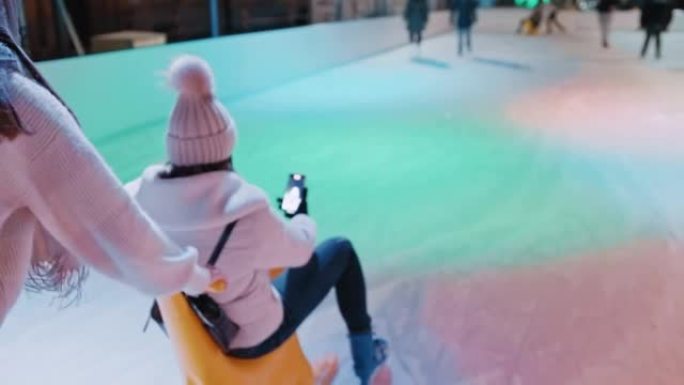 女人推她的朋友坐在溜冰场的雪橇上的后视图