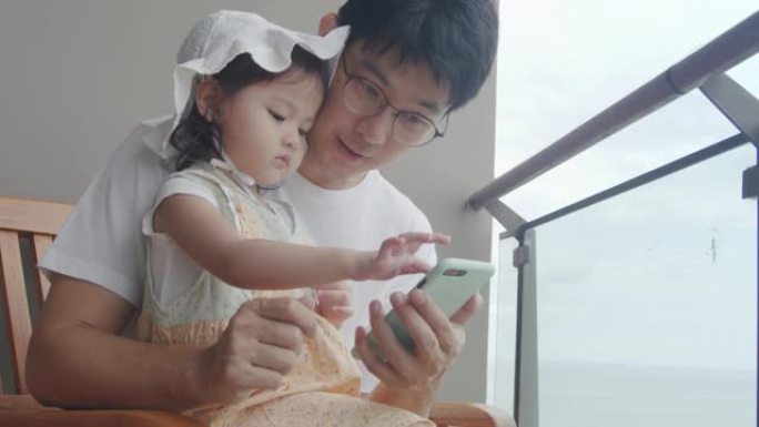 亚洲父亲和女儿一起看智能手机。开朗的年轻成年父母与孩子一起使用手机。