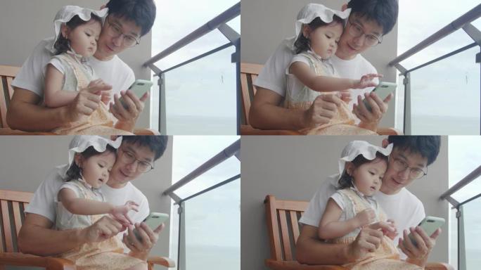 亚洲父亲和女儿一起看智能手机。开朗的年轻成年父母与孩子一起使用手机。