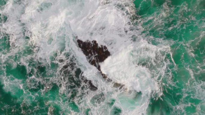 海鸥的空中慢动作镜头飞越绿松石海，波浪在石头上折断。带有白色泡沫的海上或海洋冲浪