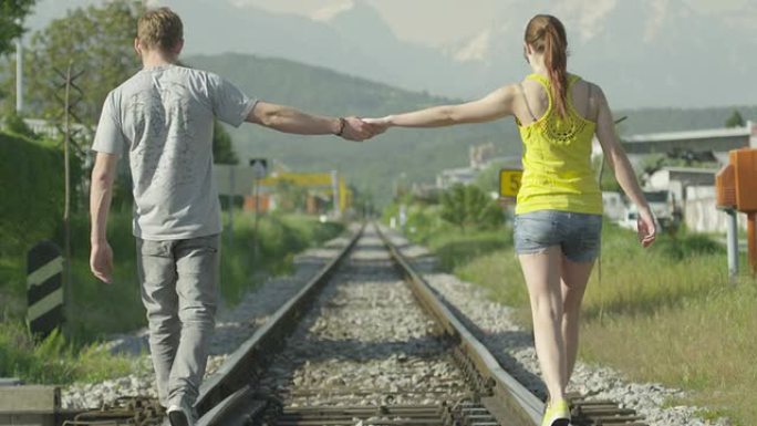 慢动作: 夫妻在铁轨上行走时牵手