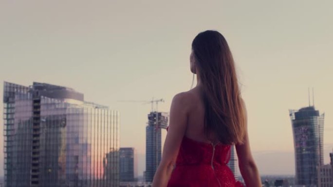 解放的女人在屋顶上跳舞。穿着红色神话般的连衣裙欣赏城市全景