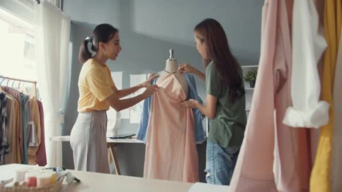 两位专业的亚洲开朗女士时装设计师团队合作，在面料上休闲别针分享创意，在商店假人身上创造漂亮的服装。女