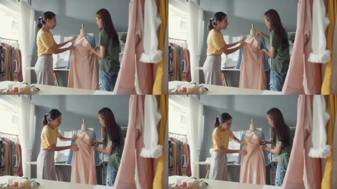 两位专业的亚洲开朗女士时装设计师团队合作，在面料上休闲别针分享创意，在商店假人身上创造漂亮的服装。女