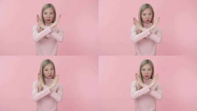 工作室肖像，年轻美丽的亚洲女子穿着粉红色长袖t恤，显示停止或拒绝标志，并在粉红色背景下对着镜头不开心