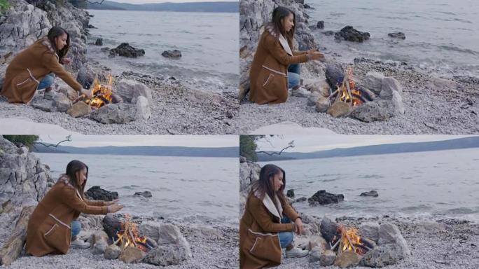 年轻女子将木头和温暖的手放在篝火上