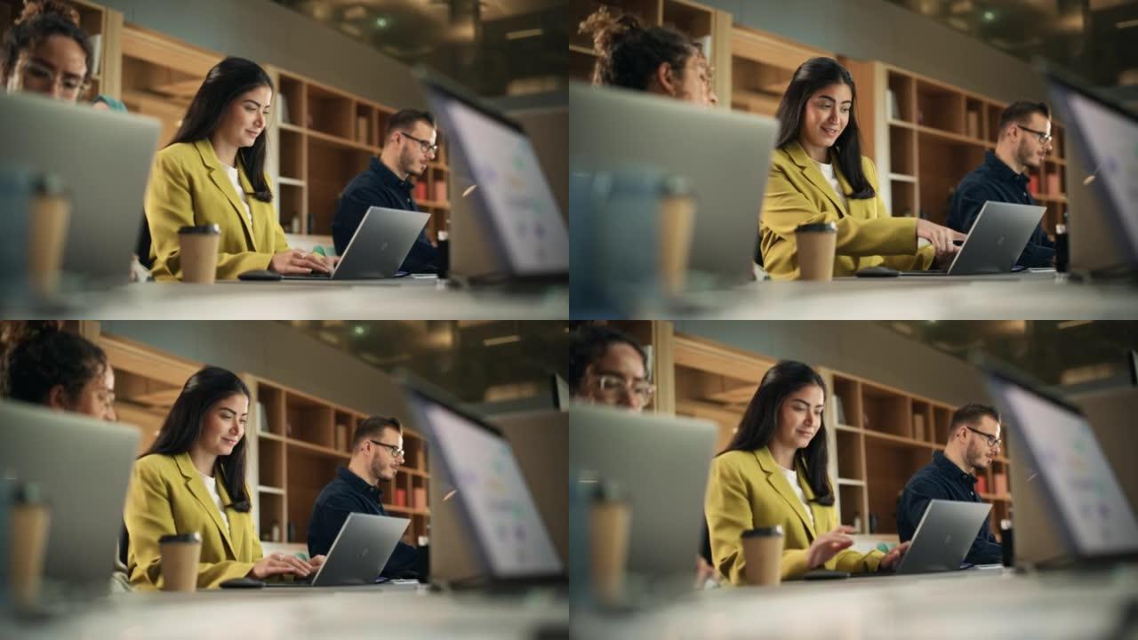 在活跃的当代办公室中使用笔记本电脑的多元化创意团队成员。年轻的女性媒体关系经理致力于品牌创新战略并与