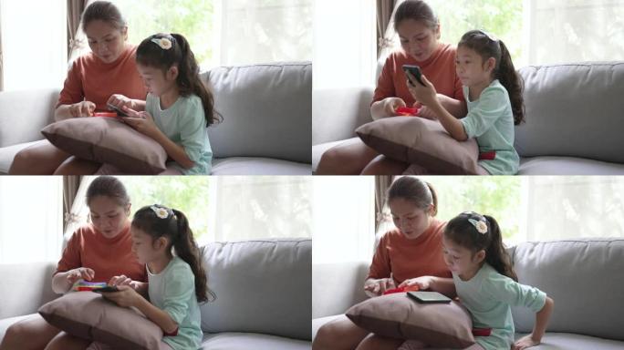 亚洲妈妈和女儿在家里的客厅沙发上玩智能手机