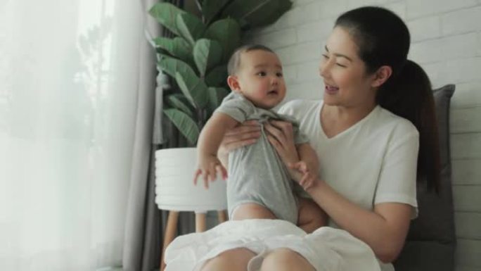 快乐的成年亚洲妈妈在家里抱着和她可爱的新生男婴玩耍。玩耍有助于建立牢固的关系