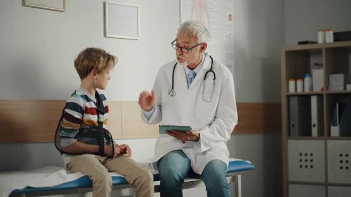 友好的中年家庭医生与一个小男孩与手臂支撑和显示测试结果的平板电脑。快乐的医疗保健医生在医院给一个手臂