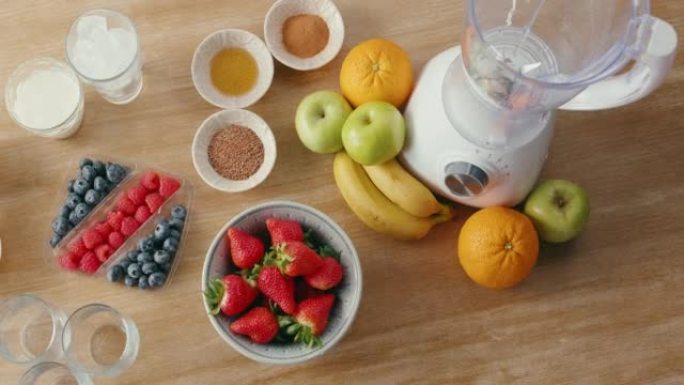 木桌上的新鲜农产品和健康奶昔配料的俯视图。水果，杏仁和其他成分以及用于制作冰沙的搅拌机。健康节食和营