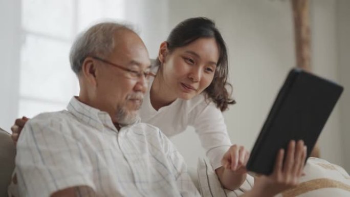 资深亚洲父亲和中年女儿在客厅的数字平板电脑上使用社交媒体