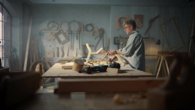 中年木匠戴上眼镜，阅读蓝图并开始组装木椅的零件。时尚的家具设计师在阁楼空间的工作室工作，墙壁上有工具