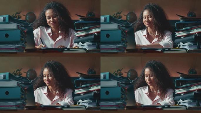 快乐忙碌的年轻混血女老板，会计经理微笑着在家里的桌子上工作，周围有许多文件。