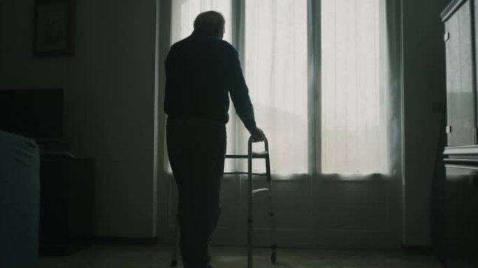 一位老人的电影镜头正踩着高跷走向窗户，打开窗帘向外面看。生活概念、医疗保健、退休、残疾、寄宿房