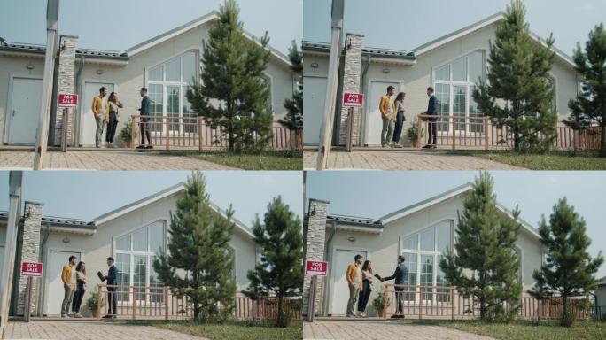 快乐的夫妇站在户外美丽的郊区房子附近与房地产经纪人交谈
