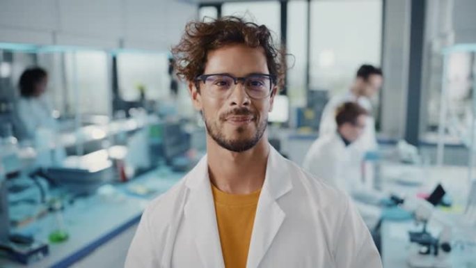 医学科学实验室: 穿着白色外套的年轻拉丁科学家戴上眼镜，交叉双臂，看着相机微笑。多元化的专家团队。中