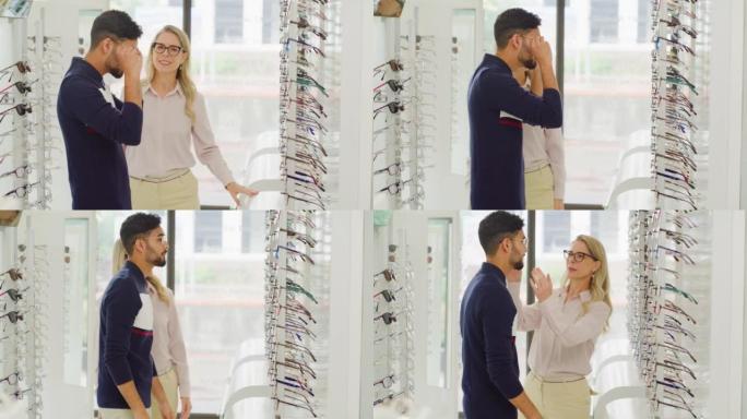 友好的配镜师或验光师帮助顾客选择商店货架上的眼镜。乐于助人的成熟女人和店主协助男人在她的眼镜店里选择