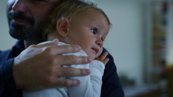 一个年轻快乐的微笑父亲的电影特写镜头将他的儿子蹒跚学步的男婴抱在怀里，拥抱着他，同时在家里享受时光。