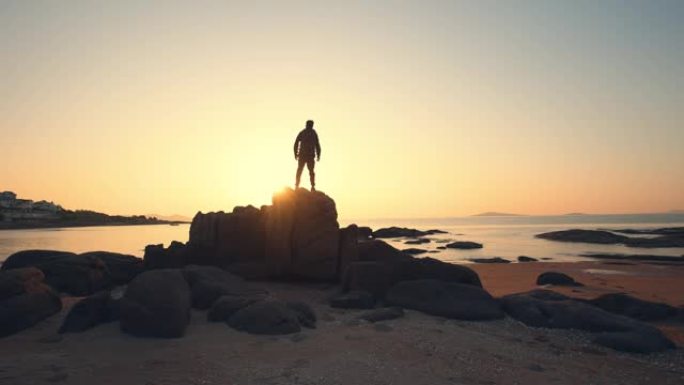 站在岩石上看海上日出的年轻人
