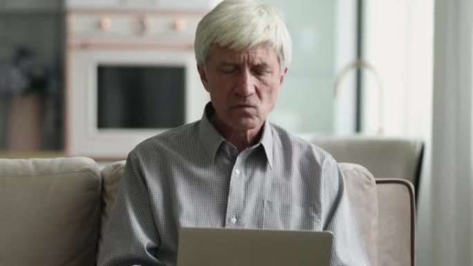 年长的沉思认真的专心男人坐在笔记本电脑的沙发上