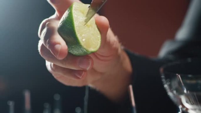 专业调酒师的特写镜头是在酒吧或迪斯科俱乐部为顾客准备含冰块的酒精鸡尾酒时挤压石灰。