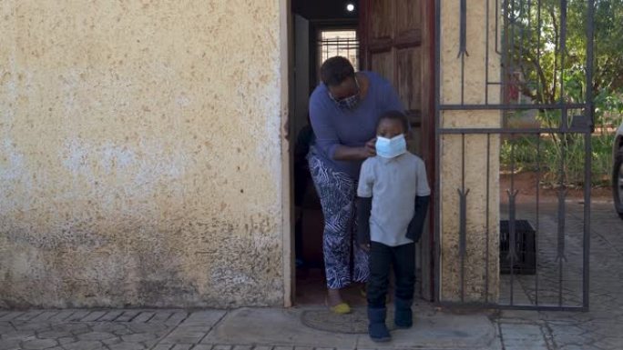 南非黑人母亲在离家前给她可爱的小儿子戴上口罩，以防止新型冠状病毒肺炎冠状病毒大流行