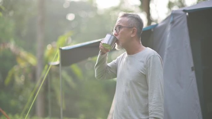 亚洲中国高级男子在露营帐篷外喝杯热饮享受早晨的新鲜感
