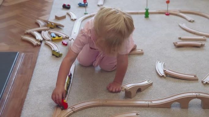 家里的年轻女孩在地毯上玩木制火车玩具