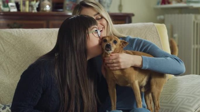真实的照片，快乐的年轻女子与患有唐氏综合症的妹妹和他们的狗在家里玩得开心，在镜头前微笑。爱的概念，家
