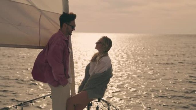 SLO MO年轻夫妇在日落时航行的帆船甲板上聊天