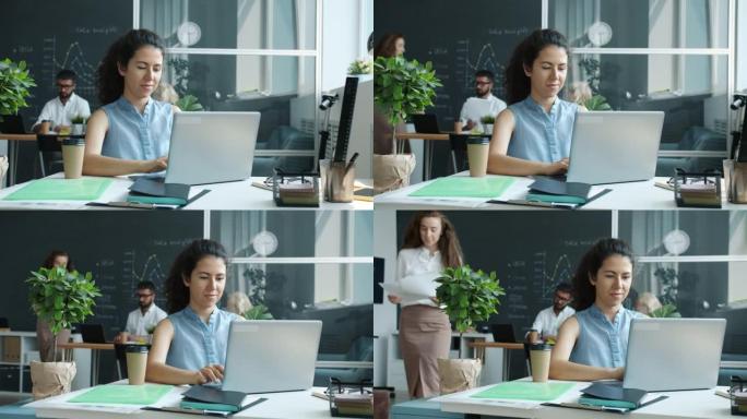 女性员工使用笔记本电脑打字坐在共用玻璃墙办公室的办公桌上