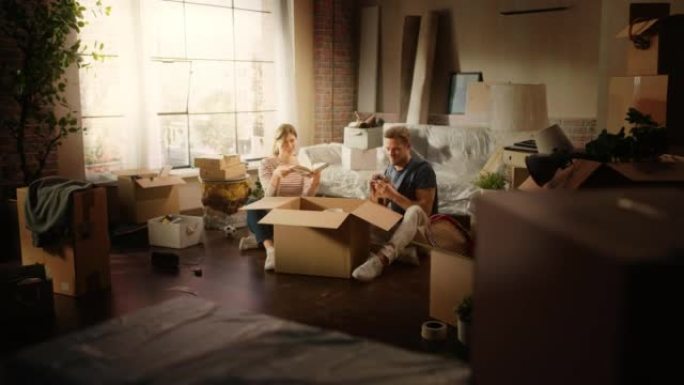快乐的房主搬进来: 可爱的夫妇坐在舒适公寓的地板上打开纸板箱。抵押贷款，房地产，年轻家庭的甜蜜之家。
