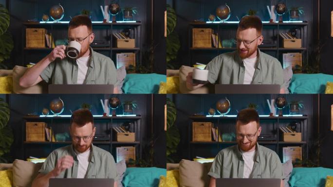 快乐的年轻聪明的红头发自由博客作者在眼镜上微笑，用笔记本电脑在沙发上在线工作喝咖啡。