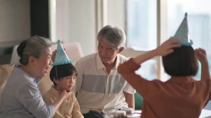 亚洲华裔男子帮助父亲戴上派对帽准备在家客厅庆祝生日