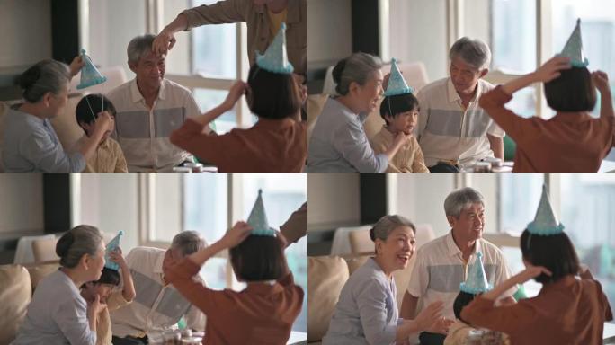 亚洲华裔男子帮助父亲戴上派对帽准备在家客厅庆祝生日