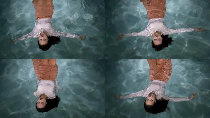 萧条时代。年轻美丽悲伤的混血女人漂浮在浅水面慢动作上的电影俯视图。