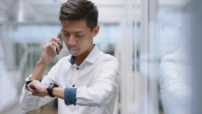 年轻的亚洲商人使用智能手机打电话聊天手机推销员享受与客户交谈看着手表在公司办公室工作场所4k