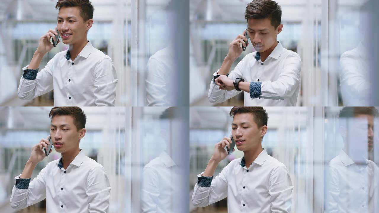 年轻的亚洲商人使用智能手机打电话聊天手机推销员享受与客户交谈看着手表在公司办公室工作场所4k