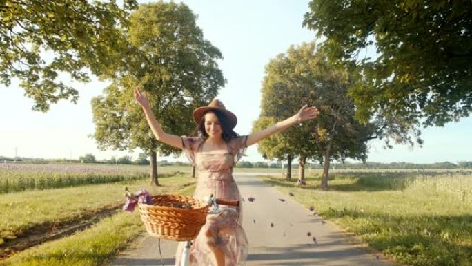 慢动作年轻女子在骑自行车穿过树线路时扔花